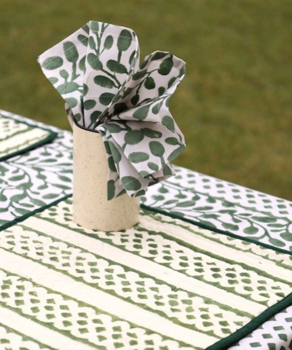 Green nd white dinner napkin layed on a table in a tumbler. the table is layed with an organic cotton table cloth and a set of 4 reversible table mats in the middle of a natural meadow for a sensuous retreat.