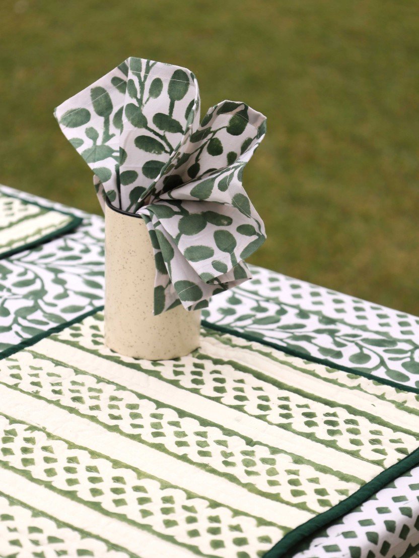 Green nd white dinner napkin layed on a table in a tumbler. the table is layed with an organic cotton table cloth and a set of 4 reversible table mats in the middle of a natural meadow for a sensuous retreat.