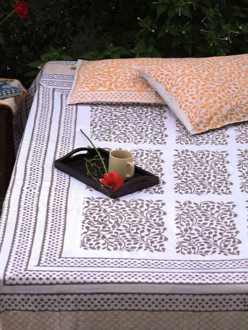 Brown and white king size bed sheet with two reversible tan pillow covers adorned on a double bed in the middle of a green meadow to enhance slow morning tea.