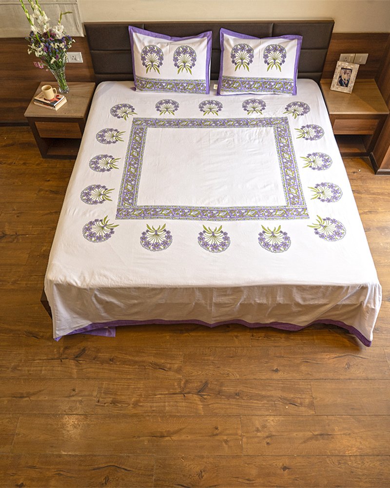 A luxurious king size double bed draped in kalaaai's organic cotton bed sheet in white and purple colors hand block printed in minimalistic floral design