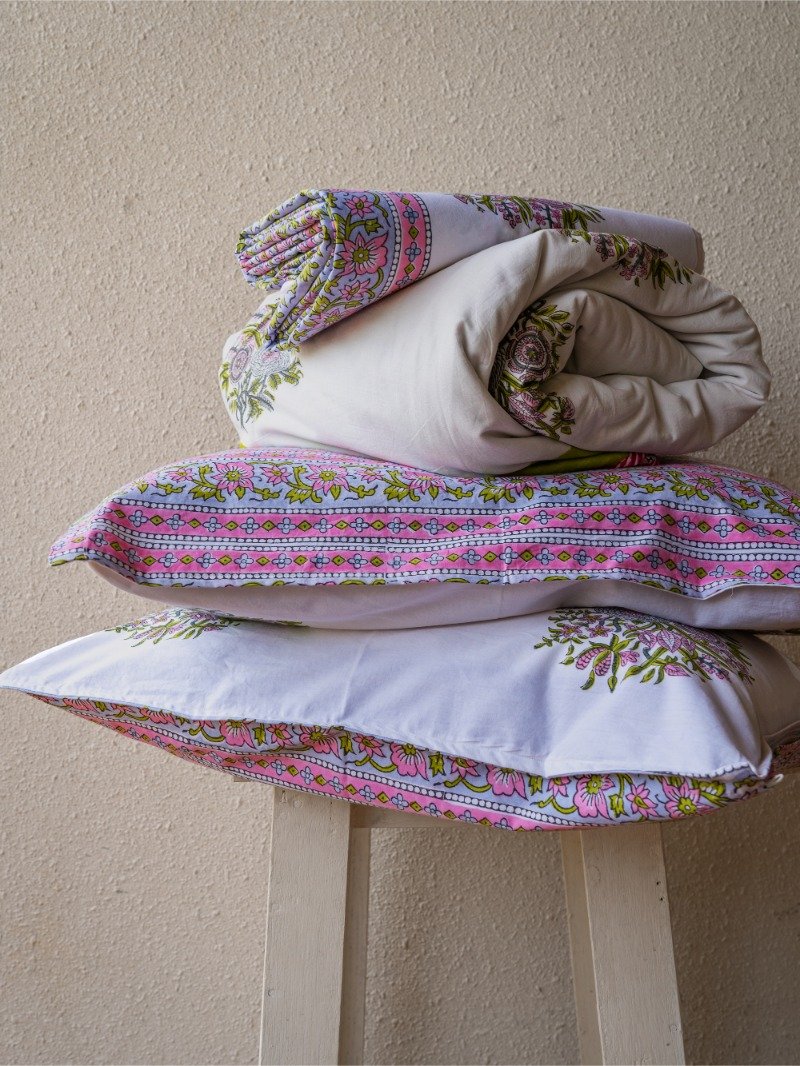 Assortment of organic cotton bed sheet, 2 pillow covers and an ac quilt in coordinating design and color kept on a stool.