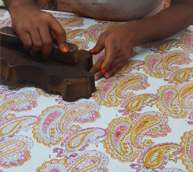 Artisan printing a beautiful paisley design in yellow and pink colors in jaipur, sanganer, India