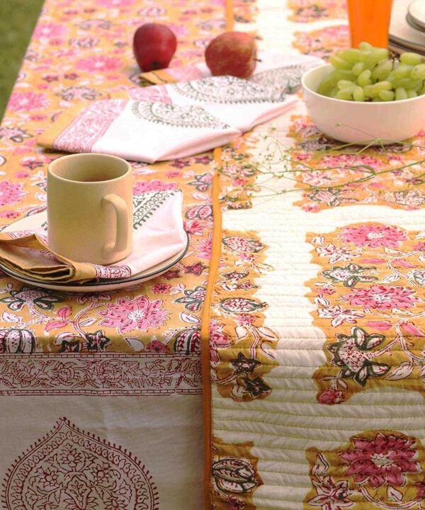 Kalaaai hand crafted organic cotton contemporary table runner in reversible floral design set on a dining table showing Ochre side with beautiful floral design in ochre and pink colors. this is set on a coordinating ochre tale cloth with coordinating napkins for a special healthy breakfast.