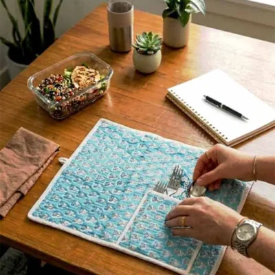 Kalaaai Turquoise Floral Buti Roll-Up Travel Dining Mat Set with hand block printed floral shrub motifs, quilted cotton mat, spoon, fork, cotton napkin, and built-in cutlery pocket. A heritage-inspired eco-friendly lifestyle accessory for travel and office lunches.