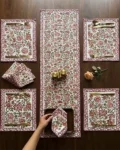 Top view of a beautifully styled dining table featuring Kalaaai Jaipur's hand block printed floral table linen set with coordinating table runner, placemats, and napkins in red, peach, and green.