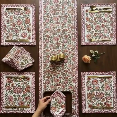 Top view of a beautifully styled dining table featuring Kalaaai Jaipur's hand block printed floral table linen set with coordinating table runner, placemats, and napkins in red, peach, and green.